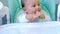 A hungry baby is gnawing on a plastic spoon at the table on a high chair. Teething, whims, itchy gums, introduction of