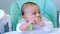 Hungry baby is gnawing on a plastic spoon at the table on a high chair. Teething, whims, itchy gums, introduction of