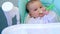 A hungry baby is gnawing on a plastic spoon at the table on a high chair. Teething, whims, itchy gums, introduction of