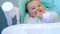 A hungry baby is gnawing on a plastic spoon at the table on a high chair. Teething, whims, itchy gums, introduction of