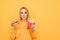 Hungry cute girl with french fries in his mouth, holding a burger in his hands and looking in camera, isolated on a yellow