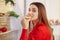 Hungry female student eats snack, stands in front of opened refrigerator full of vegetables, looks directly into camera, dressed i