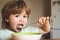 Hungry little boy eating. Cheerful baby child eats food itself with spoon. Tasty kids breakfast. Baby eating food on