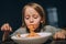 Hungry little girl appetite eating the bolognese pasta sucking it up to mouth in the low light kitchen table