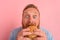 Hungry man with beard and tattoos eats a sandwitch with hamburger
