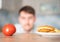 Hungry man chooses between a cheeseburger and a tomato. Fast food or vegetable diet. The temptation of junk food