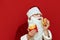 Hungry Santa Claus isolated on red background with burger and french fries in hands. Man in santa costume eating burger. Isolated