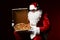 Hungry Santa Claus is looking inside the box with big hot tasty pizza, showing us. New year Christmas fast food