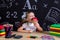 Hungry schoolgirl sitting at the desk with books, school supplies, holdingand biting the red apple