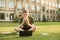 Hungry student sitting on the lawn on the back of the university building, eating a sandwich and looking at the screen of a laptop