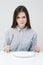 Hungry thin girl sitting at the table in front of an empty plate with a knife and fork.