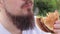 Hungry young man with a beard eats a delicious burger