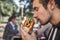 Hungry young man enthusiastically sniffing his burger while sitting at the restauraunt terrace. His eyes are closed