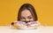 Hungry young woman peeking out of table looking at donuts