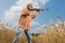 Hunter in cap and sunglasses aiming a gun at field