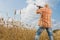 Hunter in cap and sunglasses aiming a gun at field