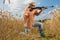 Hunter on cap and sunglasses aiming a gun at field