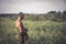 Hunter man with shotgun standing in rural field in tall reed grass during hunting season in hot summer day