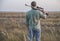 Hunter stands in the field with his back putting the gun on his shoulder