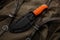 A hunting knife with a orange rubberized grip on a khaki canvas backpack. Weapons for self-defense and survival