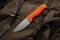 A hunting knife with a orange rubberized grip on a khaki canvas backpack. Weapons for self-defense and survival