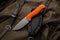 A hunting knife with a orange rubberized grip on a khaki canvas backpack. Weapons for self-defense and survival