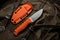 A hunting knife with a orange rubberized grip on a khaki canvas backpack. Weapons for self-defense and survival