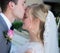 Husband kissing the forehead of the wife surrounded by greenery with a blurry background