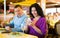 Husband looking distrustfully at his wife with smartphone in restaurant