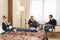 The husband and wife and the children in the hotel room. A children are sitting on the bed, parents on chairs. Young