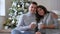 Husband and wife holding large white cups in their hands on his home couch in morning on background of xmas tree