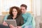 Husband and wife sitting on sofa at home looking at tablet