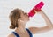 Hydration during workout. Millennial athlete drinking water from sports bottle indoors