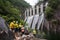 Hydroelectric dam with cascading water, workers in safety gear inspecting the infrastructure, surrounded by lush greenery