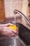 hygiene, health care and safety concept - close up of man hands washing lemon fruit in kitchen at home