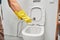 Hygienic shower in a female hand, close-up on the background of the toilet. Women& x27;s hands in yellow rubber gloves on