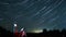 Hyperlapse of stars rotating in the night sky and people standing on the meadow and watching them