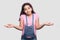 I don`t know. Portrait of confused brunette young girl in casual style, pink t-shirt and blue overalls standing, raised arms and