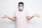 I don`t know. Portrait of confused young man with surgical medical mask in striped t-shirt standing with raised arms and dont kno