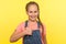 I like it! Portrait of charming pleased little girl with braid in denim overalls smiling at camera and gesturing thumbs up