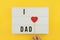 I love Dad text on white lightbox with wooden heart on yellow background