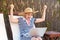 I am winner! Portrait of positive young adult blogger woman in hat and dress sitting on cozy sunbed with laptop and celebrate