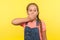 I won`t tell! Portrait of scared little girl with braid in denim overalls covering mouth with hand, afraid to say secret