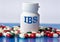 IBS - medical acronym on a white jar against the background of randomly scattered tablets