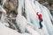 Ice climber dressed in warm winter climbing clothes, safety harness and helmet climbing frozen waterfall using two Ice climbing