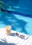 Ice coffee Cyprus Frappe Fredo against blue clear water of the swimming pool, on white table, with metal straw . Summer