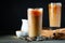 Ice coffee in a tall glass with cream poured over, ice cubes and beans on a old rustic wooden table. Cold summer drink with tubes