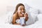 Ice cream in bed. Smiling african american woman wrapped in blanket and eating