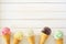 Ice cream cone bottom border with a variety of flavors, top down view over a white wood background