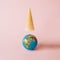 An ice cream cone hangs over a globe on a pastel beige background. Minimal summer and travel style.